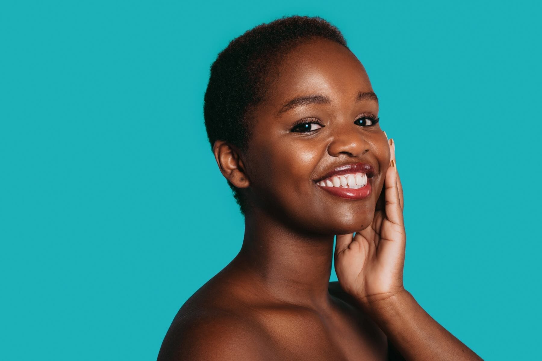 African-American naked woman touching her face and looking at camera isolated on blue background with copy space. Beauty face. Beauty treatment. Girl facial treatment.